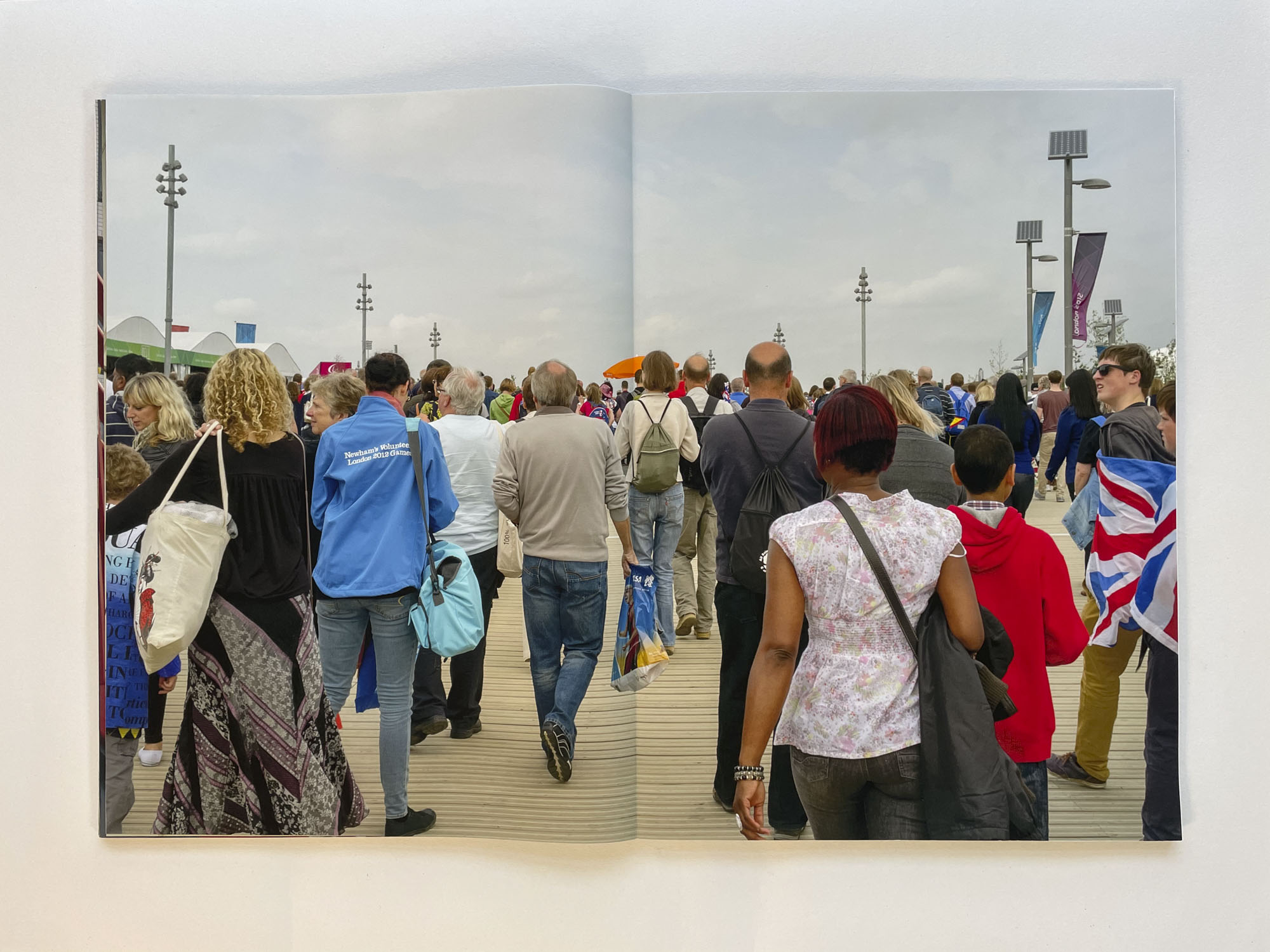 a crowd of people are walking away from the viewer, one of them is wrapped in a Union Jack