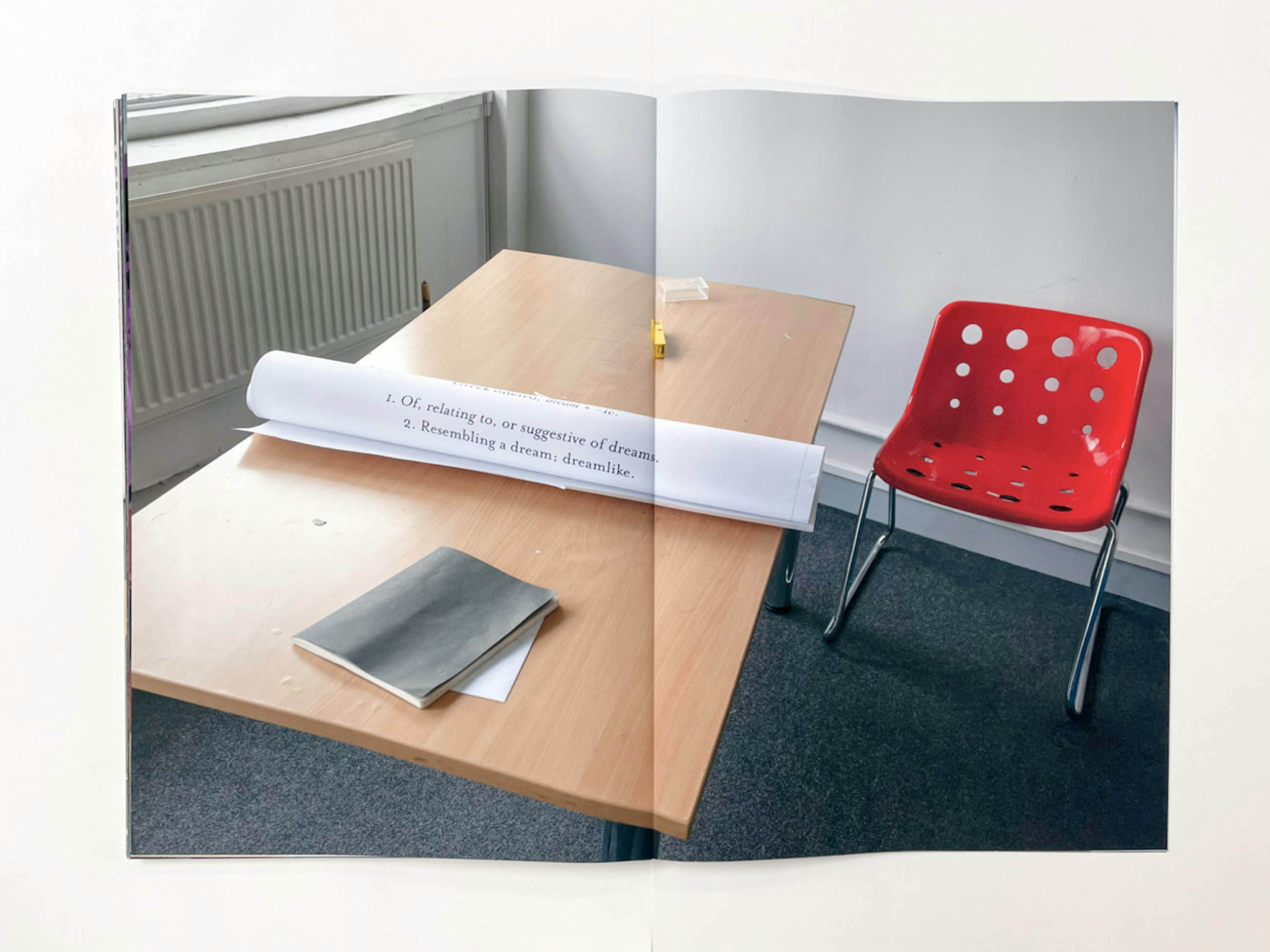 a red plastic chair beside a formica table on which a rolled up piece of paper has the words 1. of, relating to, or suggestive of dreams, 2. resembling a dream; dreamlike.