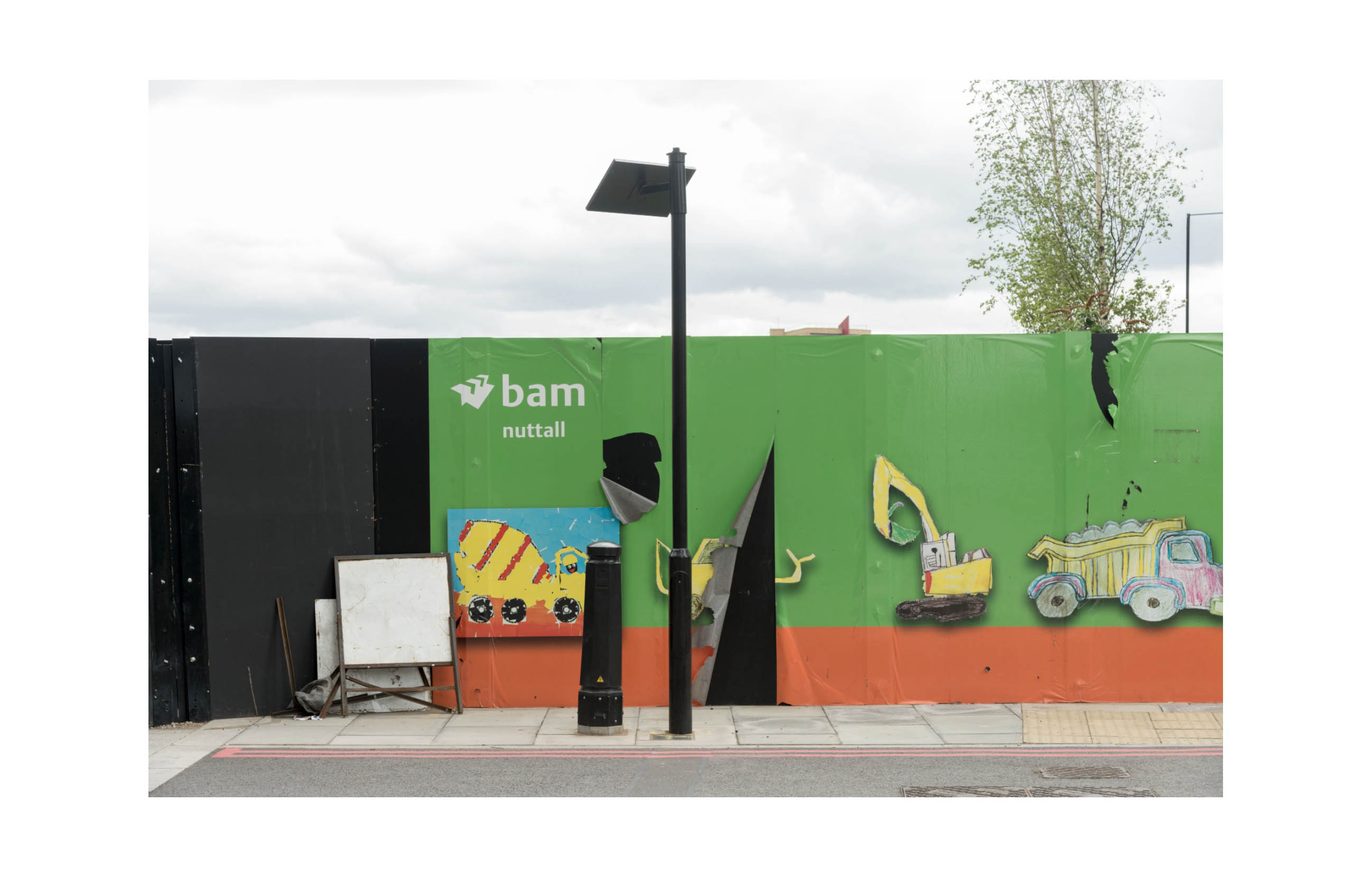 a hoarding shows children's drawings of construction equipment, the material is torn and peeling away'