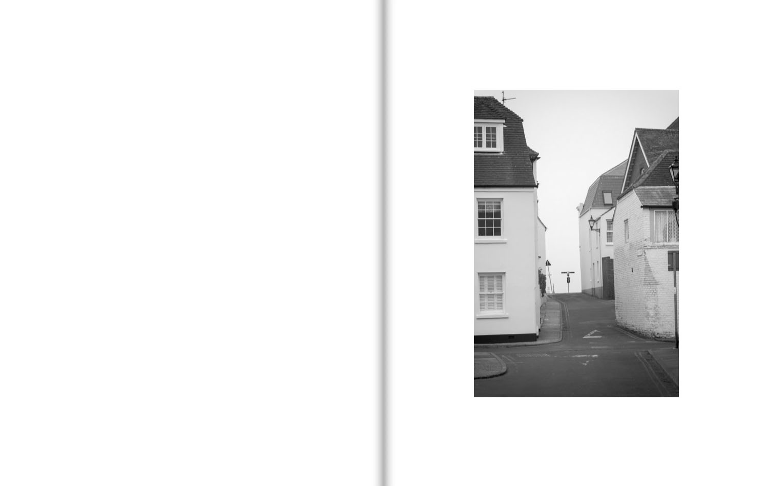 A narrow street gently rises between white houses, at the top of the slope a signpost is silhouetted against the sky.