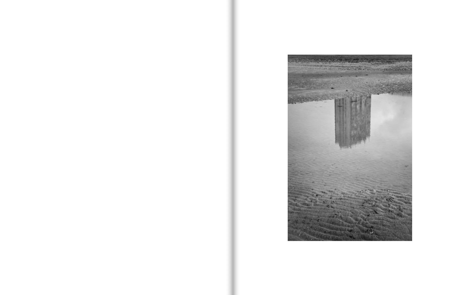 A tower block is reflected in a pool on a sandy beach that is shaped into rivulets by the tide.