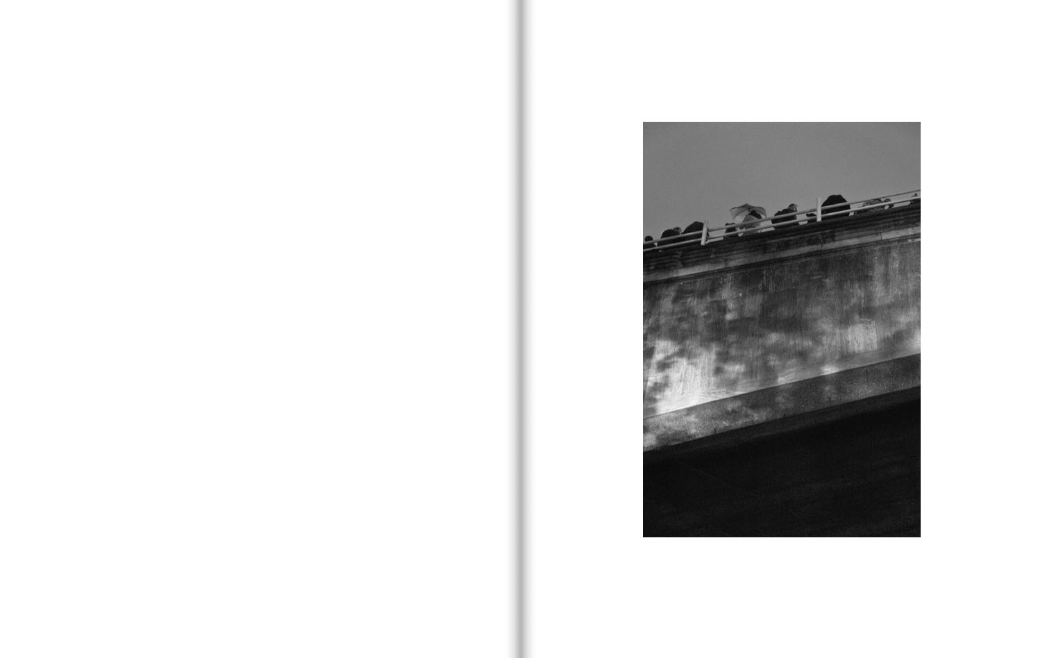 Seen from below, a number of people lean their backs against the railings of a large bridge.