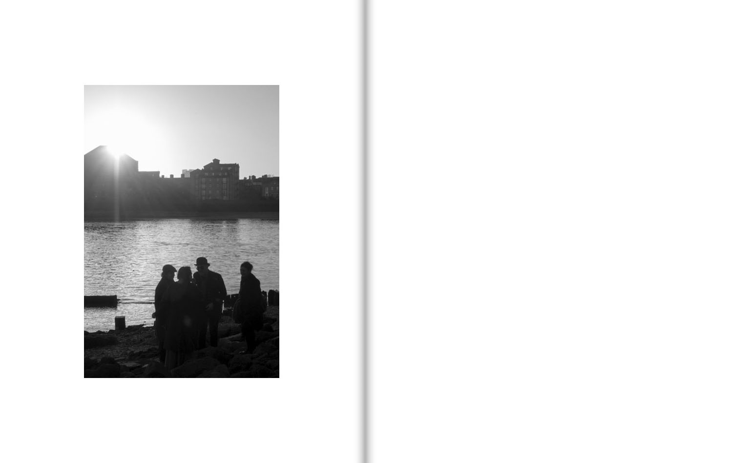 Four people stand by a river silhouetted by a sun that is rising (or setting) behind buildings on the opposite bank.
