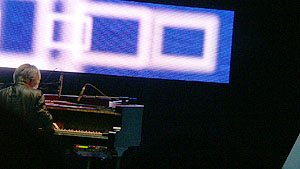 Image of Sakamoto playing with video screen behind him