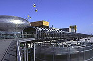 image of futuristic building complex with enclosed pedestrian walkway, mostly silver, a large dome to the left